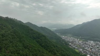 Sisli vadideki küçük bir kasabaya giden yeşil dağın havadan görünüşü. Yüksek kalite 4k görüntü