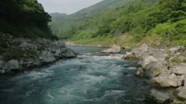 Güneşli bir günde, nehirdeki küçük akıntıların üzerinden kanyon boyunca alçaktan uçmak. Yüksek kalite 4k görüntü