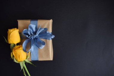 Bir hediye ve siyah arka planda iki sarı gül.