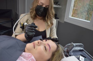 Genç bir kıza kalıcı kaş makyajı yapan bir kozmetolog.