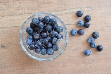 Ahşap arka planda donmuş yaban mersinli cam bir kase.