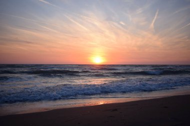 Çalkantılı okyanusta sahilde güzel bir gün batımı. Turuncu ve mavinin tonları.