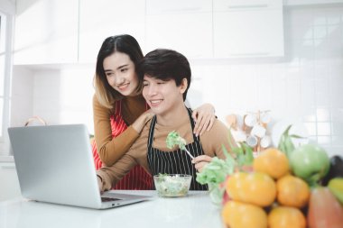 Genç Asyalı çift evdeki mutfakta online eğitim izliyorlar, sağlıklı bir yaşam tarzı var..