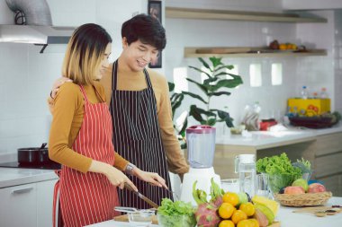 Asyalı genç bir çift evde sebze doğrayan bir yemek hazırlıyor, sağlıklı bir yaşam tarzı..