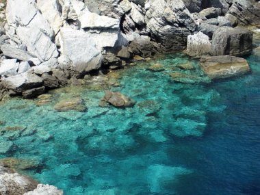 Kayalık bir kıyının arka planında parlak masmavi bir deniz, göl.