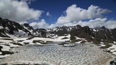 4K Zaman Hızı. Karlı dağların tepesindeki buzul gölü. Bulutlar Zaman Hızı.