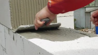 İnşaatçı malayla çalışıyor ve tuğlaya havan topu sürüyor. Adam yapı taşlarını sağlamlaştırıyor. İşçi İnşaat Evi