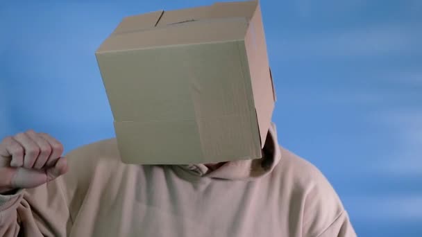 快乐的男人 头顶着一个盒子 背景是蓝色的 用纸板箱砸他的头 — 图库视频影像