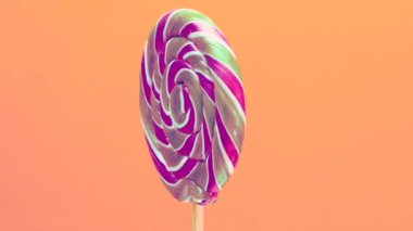 Turuncu bir arka planda, ahşap bir çubuğun üzerinde pastel renklerde yakın plan spiral lolipop. Çubukta tatlı karamel şekerler.