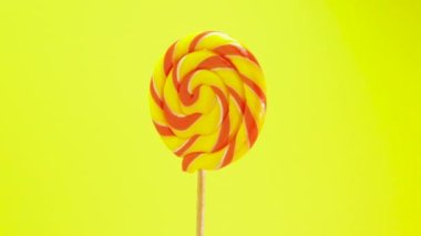 Renkli lolipop sarı arka planda dönüyor. Çubukta şeker