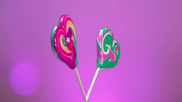 棒棒糖的混合物螺旋形旋转在粉红色的背景上 焦糖糖放在心形的棒子上 — 图库视频影像