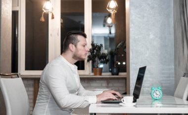 Masasındaki genç bir adam klavyeye yazı yazıyor ve evdeki elinde bir fincan kahve var. Bağımsız, çevrimiçi eğitim veya iş