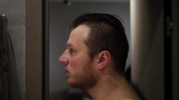 鏡の前に立っていると 若い男がバスルームで髪を結っている 手に櫛を持った髭の男 — ストック動画