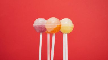 Çubukta bir sürü lolipop şekeri, kırmızı arka planda farklı aromalı karamel şekerleri karışımı.