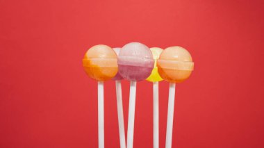Çubukta çok renkli lolipoplar, kırmızı arka planda farklı aromalı karamel şekerlemelerinin karışımı..