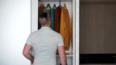 Genç adam elbiselerini dener, gardıroptan giysilerini çıkarır. Adam elbiselerini atıyor. Alışverişkolik, askıdaki modern kıyafetler.