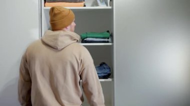 Genç bir adam dolaptan yeşil kot pantolon çıkarır, günlük kıyafet seçer. Giysilerinizi dolaptan seçin.