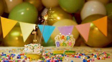 Festive background for 1 year old child's birthday, cream cupcake with burning candle and sparkler and balloons in the background. Birthday background video for 1 year old.