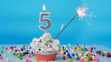 Happy birthday greetings to 5 year old child, birthday cupcake with candles and birthday decorations on blue background. Copy space