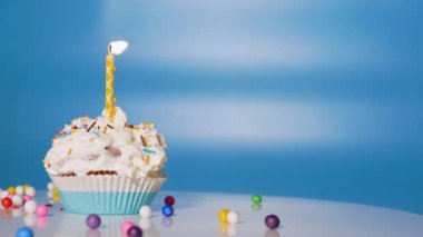 Festive cream cupcake on the turntable. Beautiful birthday greetings for a child, birthday cupcake with candles and decorations on a blue background. Copy space