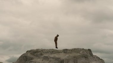Genç bir adam dağın tepesinde spor yapmaya gider, spor kıyafetleri içinde bir adam spor ipine atlar.