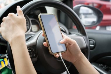 Kadın sürücü arabada akıllı telefon kullanıyor.