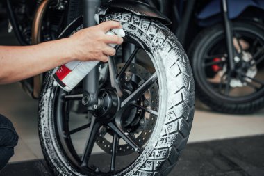 Motosiklet ya da scooter yıkayan ve lastik lastiklerinde kar köpüğü püskürten bir adam. Lastik yenileme bakımı, garajda motosiklet konseptini onarmak.