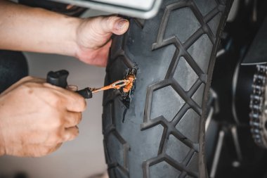 Sürücü lastik tıkaç kiti kullanır ve lastiğin yan duvarında bir delik açmaya çalışır garajda patlak bir motosiklet lastiğini tamir eder. motosiklet bakım ve onarım konsepti
