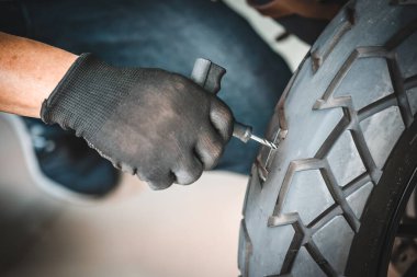 Sürücü lastik tıkaç kiti kullanır ve lastiğin yan duvarında bir delik açmaya çalışır garajda patlak bir motosiklet lastiğini tamir eder. motosiklet bakım ve onarım konsepti