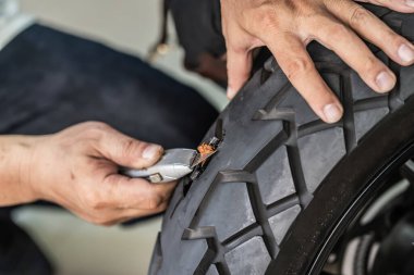 Sürücü lastik tıkaç kiti kullanır ve lastiğin yan duvarında bir delik açmaya çalışır garajda patlak bir motosiklet lastiğini tamir eder. motosiklet bakım ve onarım konsepti