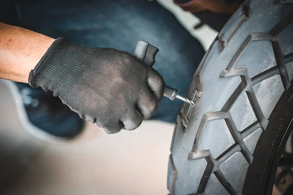 Sürücü lastik tıkaç kiti kullanır ve lastiğin yan duvarında bir delik açmaya çalışır garajda patlak bir motosiklet lastiğini tamir eder. motosiklet bakım ve onarım konsepti