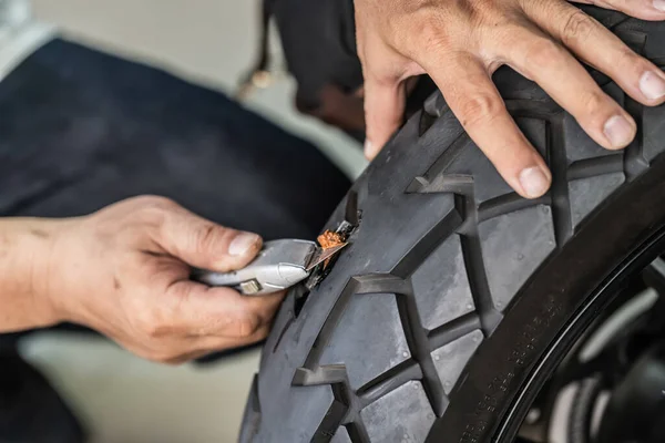 Rider use a tire plug kit and trying to fix a hole in tire\'s sidewall ,Repair a motorcycle flat tire in the garage. motorcycle maintenance and repair concept