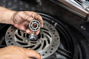 Tamirci kontrol edip, garajda çalışan, motorsiklet tekerleği bilyelerini değiştiriyor. Onarım ve bakım motosiklet konsepti. Seçici odaklanma