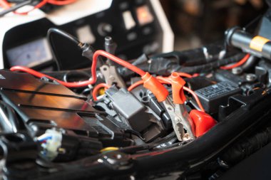 Garajda motorsiklet aküsü şarj etmek, timsah klipsine odaklanmak, motosiklet bakım ve onarım konsepti.