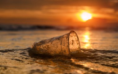 Plastik çöp bardağı deniz kıyısında günbatımı aydınlatmalı..