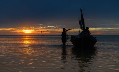 Sahildeki teknede siluet balıkçı. Gün batımında ılık, hafif ve karanlık gölgesi olan..