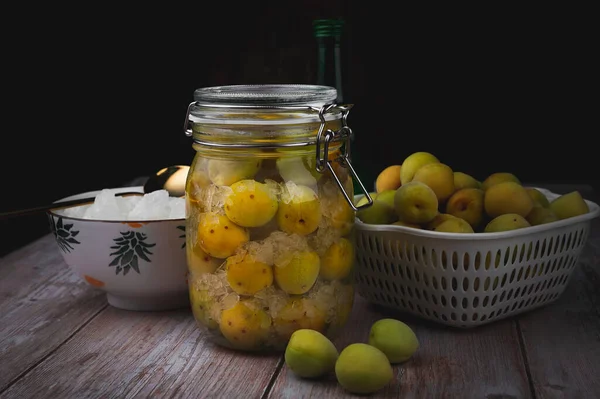 İçkili ev yapımı erik turşusu ve cam şişede kaya şekeri, ahşap tabakta düşük ışıklandırma ve koyu siyah zemin..
