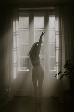 Güzel yonglu kadın sisli güzel güneş ışığında panoramik pencerenin önünde geriniyor. Yoga konsepti