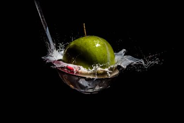 An apple splashing in cream and fruit juice on a silver spoon or ladle..