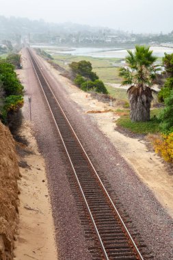 Güney Kaliforniya 'da boş tren rayları olan bir manzara. Arka planda bir kasaba ve yolda palmiye ağaçları var.