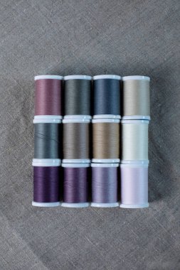 Üç sıra halinde desenli doğal keten kumaşa serilmiş 12 renkli iplik makarasının üst görüntüsünü kapat