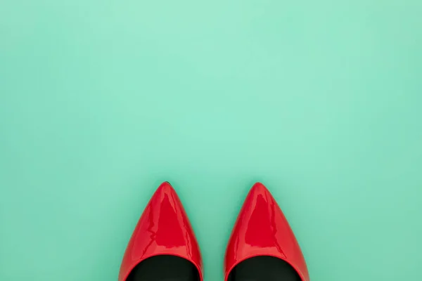 Top view of glossy red pointy toe women shoes on mint green background with copy space