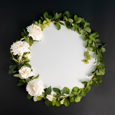 Beyaz güller açan yuvarlak çerçeveli çelenk ve siyah arka planda dallar. Minimum çiçek konsepti. Düz yatıyordu. Boşluğu kopyala.