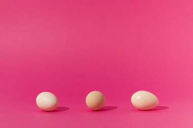 Modaya uygun pembe arka planda beyaz yumurtalarla yapılan yaratıcı bir kavram. Minimum Paskalya, bahar modeli. Çağdaş tarz. Doğal güneş ışığı ve keskin gölgeler..