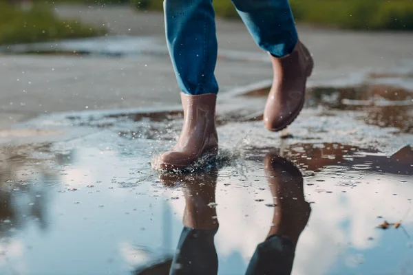 Жінка в дощових гумових черевиках ходить і стрибає в калюжу з водяними бризками і падає в осінній дощ — стокове фото