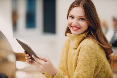 Kafe masasında bir fincan kahve ile dijital tablet kullanan güzel bir kadın.
