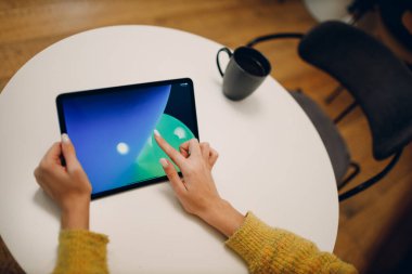 Kafe masasında bir fincan kahve ile dijital tablet kullanan güzel bir kadın.