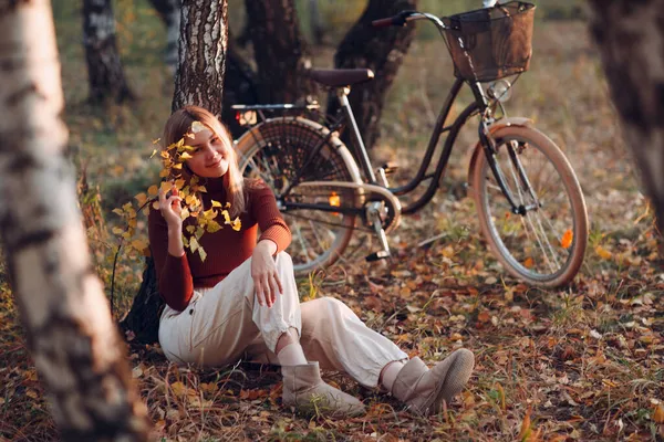 Happy active young woman sitting with vintage bicycle in autumn park at sunset — Stock Photo, Image
