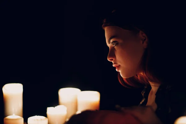 Jonge vrouw profiel portret met kaarsen licht in duisternis. — Stockfoto