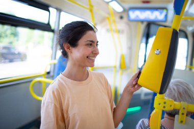 Tramvaydaki toplu taşımacılık için akıllı telefonla ödeme yapan bir kadın.